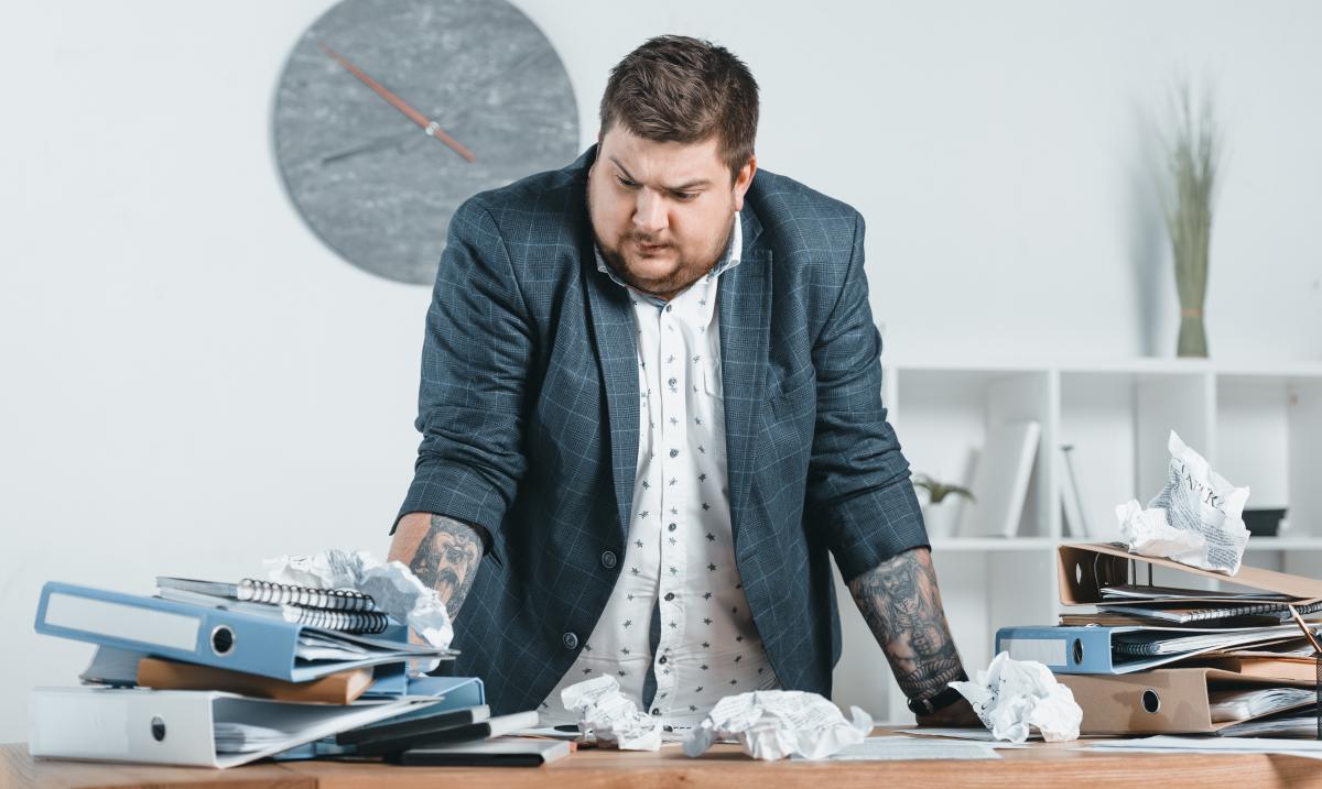 Man staat aan bureau met vele kaften administratie